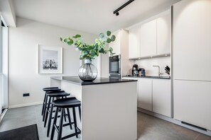 A modern kitchen with a central island, bar stools, a coffee machine, and a framed picture on the wall. - Premium vacation home Haus Deich in the dune park with terrace and sauna (List auf Sylt)