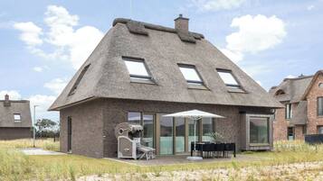 A house with a thatched roof, large windows, and a patio with outdoor furniture.