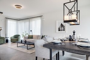 A modern living room with a dining area, featuring a sofa, chairs, a coffee table, and a dining table set for a meal. - Premium vacation home Haus Deich in the dune park with terrace and sauna (List auf Sylt)
