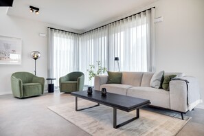 A modern living room with a sofa, two armchairs, a coffee table, and a floor lamp. - Premium vacation home Haus Deich in the dune park with terrace and sauna (List auf Sylt)