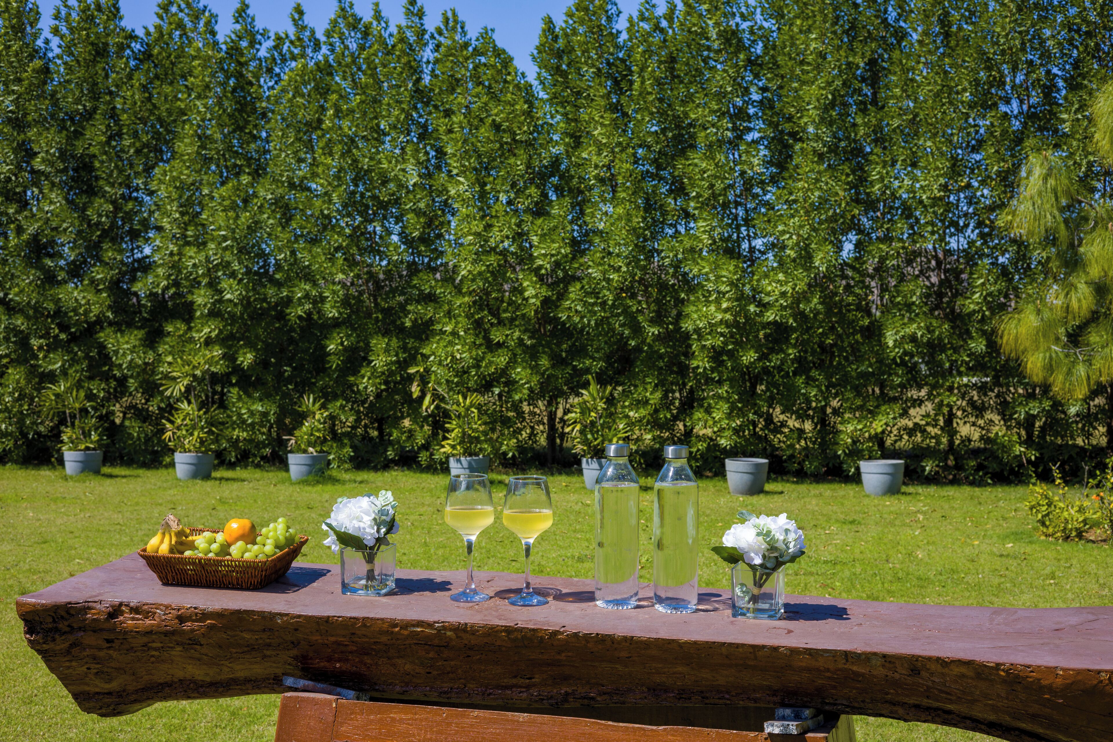A wooden table with a fruit basket, two wine glasses, and two water bottles.