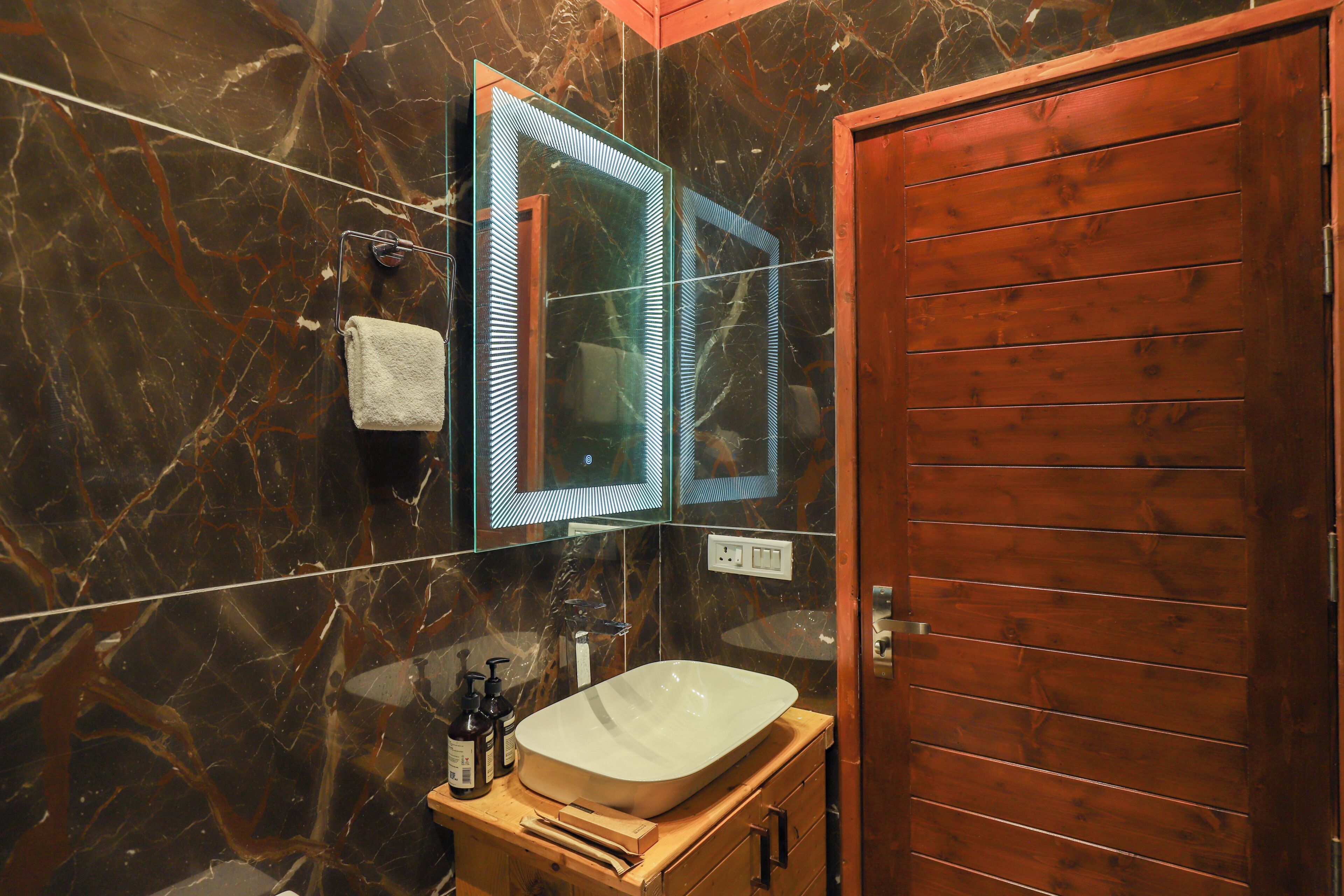 Un baño con pared de mármol, puerta de madera y lavabo blanco.
