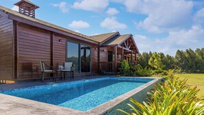 Eine Holzhütte mit Swimmingpool, einer Terrasse mit Stühlen und Blick auf die umliegende Natur.