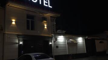 A hotel with a prominent 'HOTEL' sign, a white car parked in front, and a brick facade.