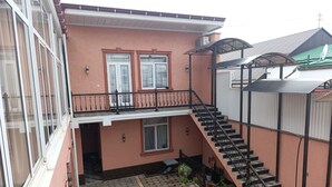 A two-story building with a balcony, a staircase, and a small garden area. - Bilol Guest House (Samarkand)