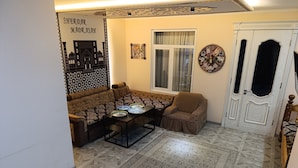 A living room with a sofa, armchair, coffee table, decorative wall art, and a patterned rug. - Bilol Guest House (Samarkand)
