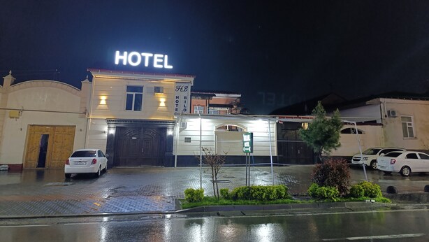 A hotel with a prominent 'HOTEL' sign, a gated entrance, and a parking area with cars. - Bilol Guest House (Samarkand)