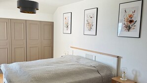 Ett sovrum med en säng, ett sängbord, en golvlampa och inramade blomstermotiv på väggen.