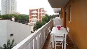 Un balcón con una mesa y sillas blancas, un pequeño jardín y vistas de edificios circundantes.