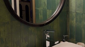 A bathroom with a round mirror, a sink, and green tiled walls. - Cozy studio Hoan Kiem lake/Opera House/Old quarter (Hà Nội)