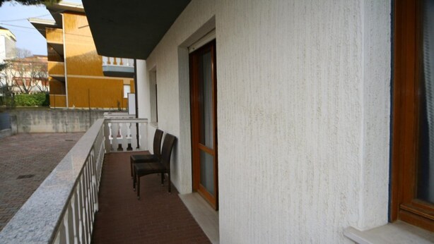 Un balcón con piso de ladrillo, barandilla blanca y ventana con marco de madera.