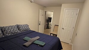 Ein Schlafzimmer mit einem Bett, Kissen, einem Flachbildfernseher und einer Tür zu einem anderen Raum.