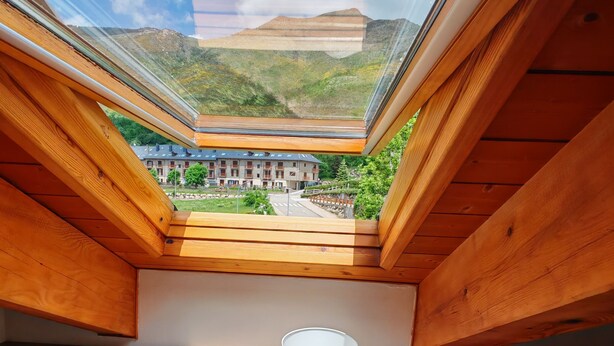 A room with two beds, a nightstand with a lamp, and a skylight offering a view of a building and mountains. - Fireplace and modern kitchen. Rustic charm - Aüt 3 (Pla de l'Ermita)