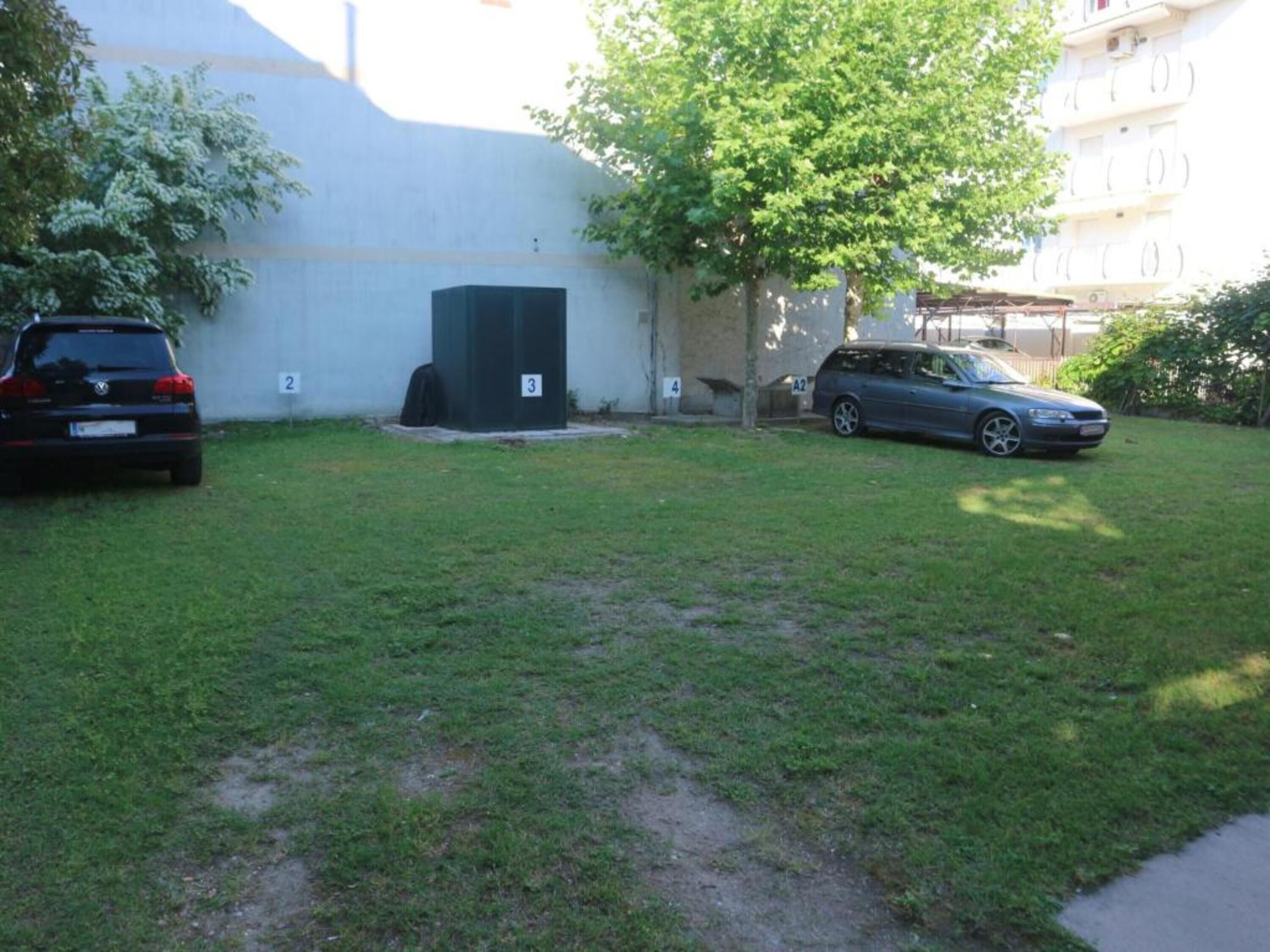 A grassy yard with two cars parked, a tree, and a building in the background.