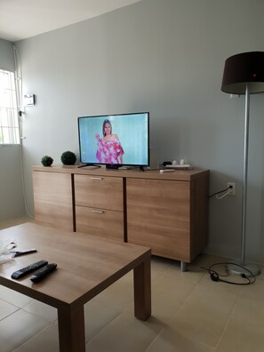 A living room with a flat-screen TV on a wooden cabinet, a coffee table with remote controls, and a floor lamp. - Casa Carmelita – Comfortable Stay in Curaçao (Willemstad)