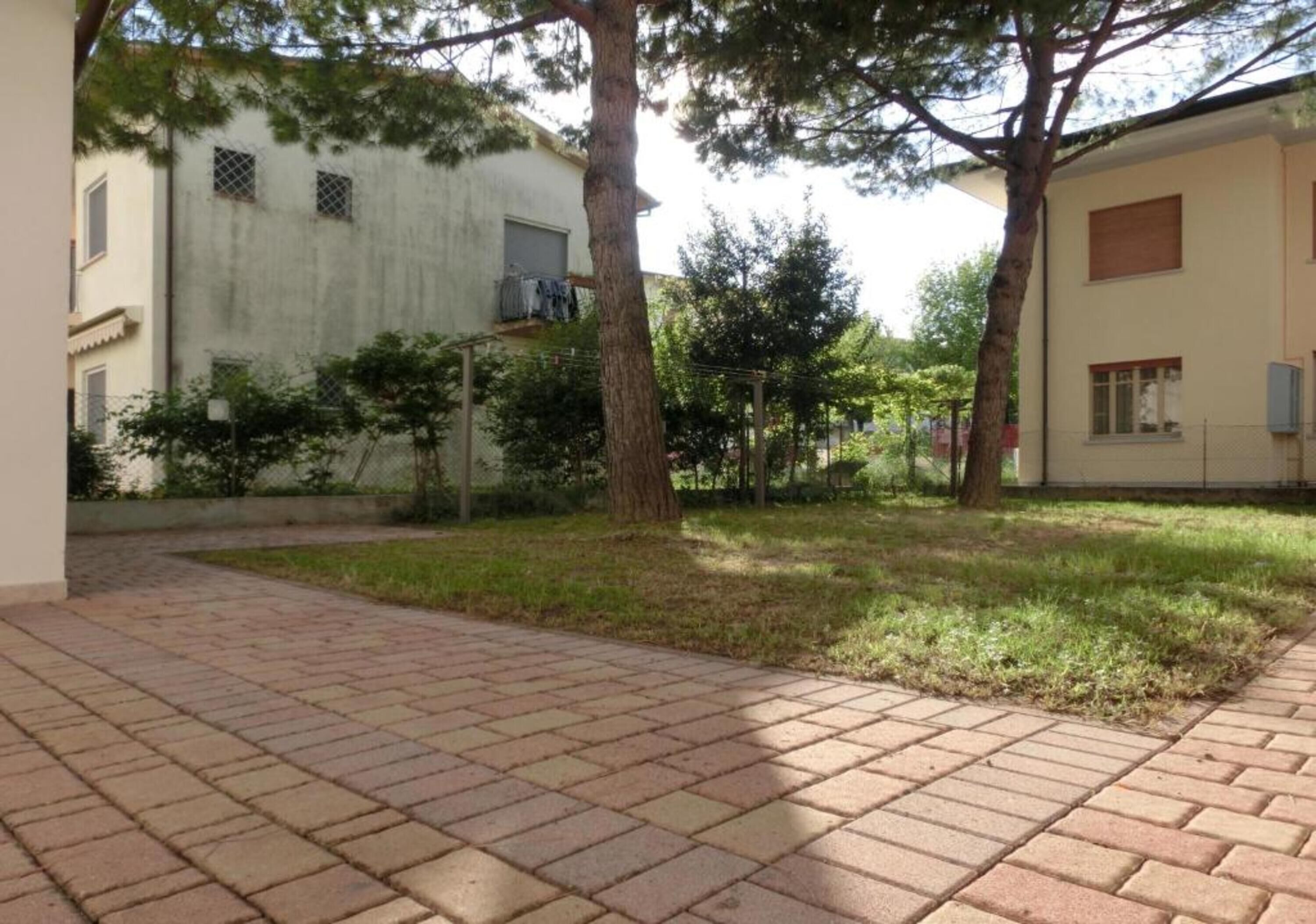 A paved courtyard with trees, a building with a window, and a wall with a fence.