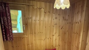 Ett rum med träpanel på väggarna, en säng, två sängbord, ett fönster och en hängande lampa.