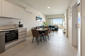 A modern kitchen with built-in appliances, a dining area with a table and chairs, and a view of the city through large windows. - The Icon 103 • Luxury 2BR • Pool & Gym • at Mythical Seas, Protaras (Paralimni)