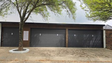 Un edificio con tres puertas de garaje identificadas con las letras D, E y F, y un árbol en frente.