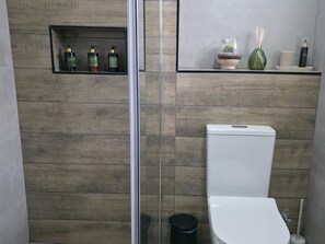 Une salle de bain moderne équipée de toilettes, d’une douche à parois de verre et d’une étagère contenant des articles de toilette.