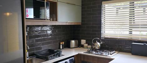 A compact kitchen with a washing machine, a stove, and a window with blinds.