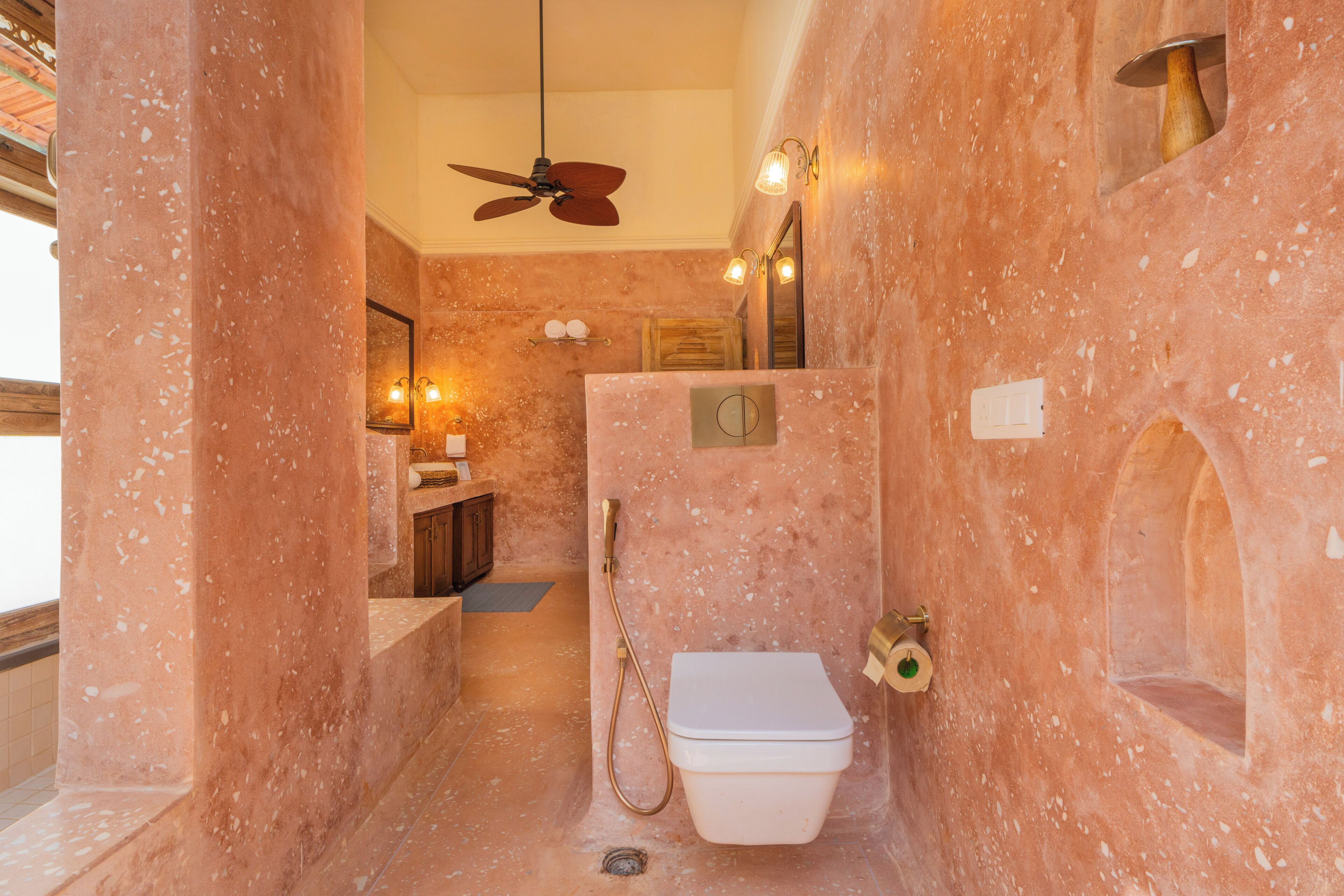 A bathroom with a marble wall, a ceiling fan, a toilet, and a shower area.