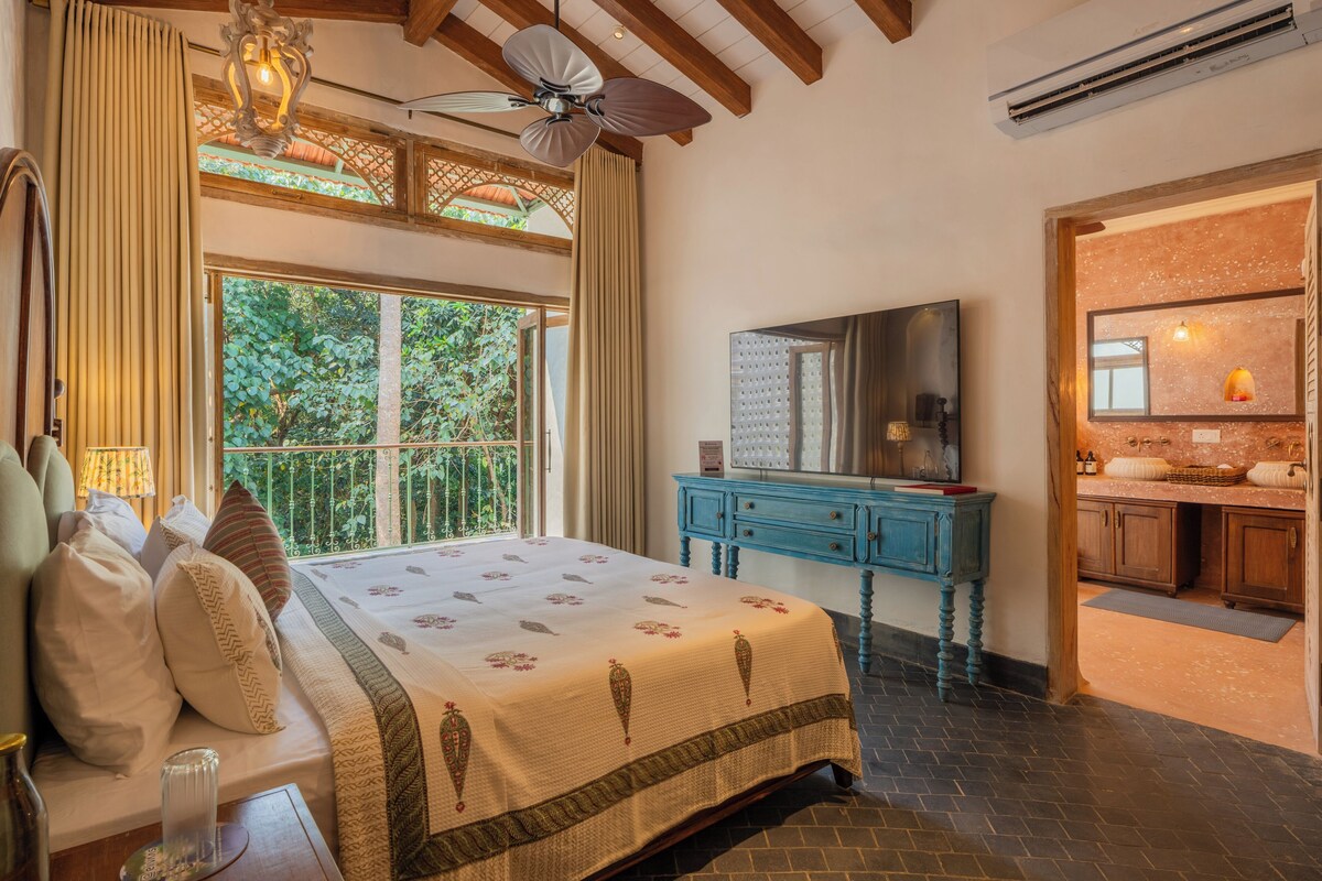 A bedroom with a bed, a ceiling fan, a window with curtains, a dresser, and a bathroom visible through an open door.