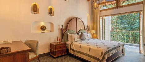 A bedroom with a bed, bedside tables, a chair, a desk, and a balcony with a view of greenery.