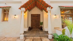 A building entrance with a tiled roof, a wooden door, and two white columns with light fixtures.