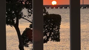 Auringonlasku veden yllä, etualalla silta ja puita.