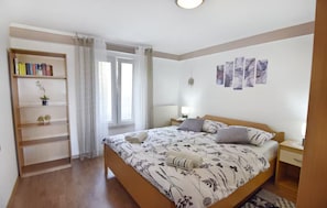 Une chambre à coucher comprenant un lit, une bibliothèque, une fenêtre avec des rideaux, une table de chevet et des œuvres d’art murales.