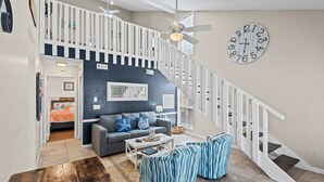 A living room with a staircase, a ceiling fan, a clock, and a sofa. - Sleeps 10, 4 Pools, Mini-golf Fun + Free Tickets: Dolphin Cruise & More! (Panama City Beach)