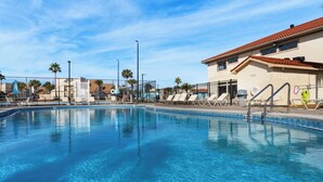 A clear swimming pool with lounge chairs and umbrellas, surrounded by a fence and palm trees. - Sleeps 10, 4 Pools, Mini-golf Fun + Free Tickets: Dolphin Cruise & More! (Panama City Beach)