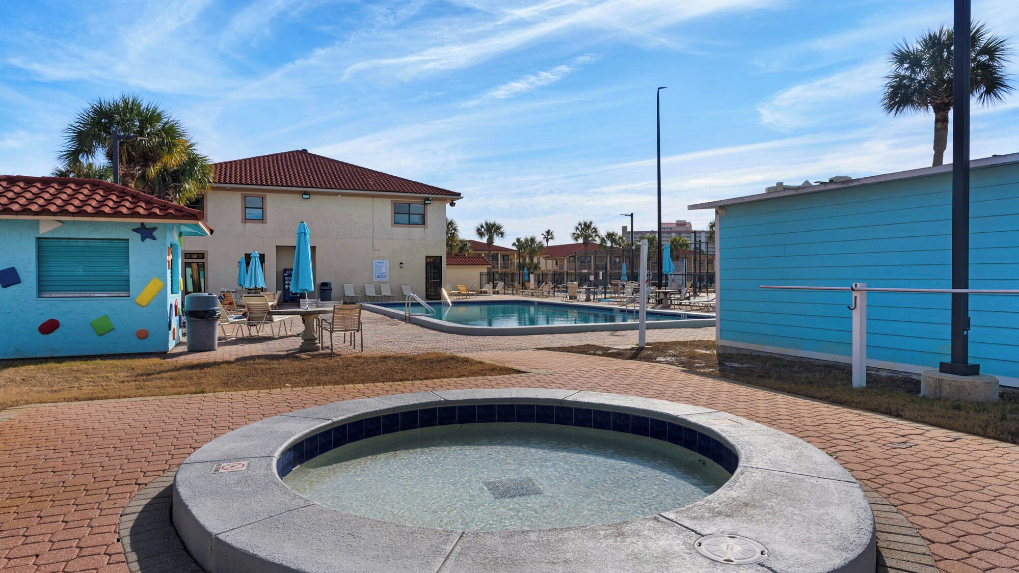 A pool area with a hot tub, lounge chairs, and umbrellas.