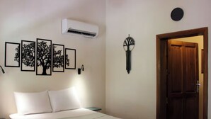 Ein Schlafzimmer mit Bett, Wand-Klimaanlage, gerahmten Baumkonturen, einer Wandlampe und einer Holztür.