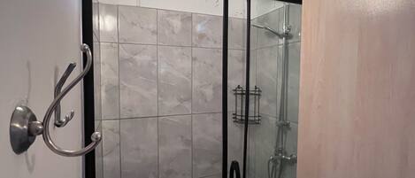 Una ducha con puerta de cristal, suelo de azulejos y un perchero de metal.