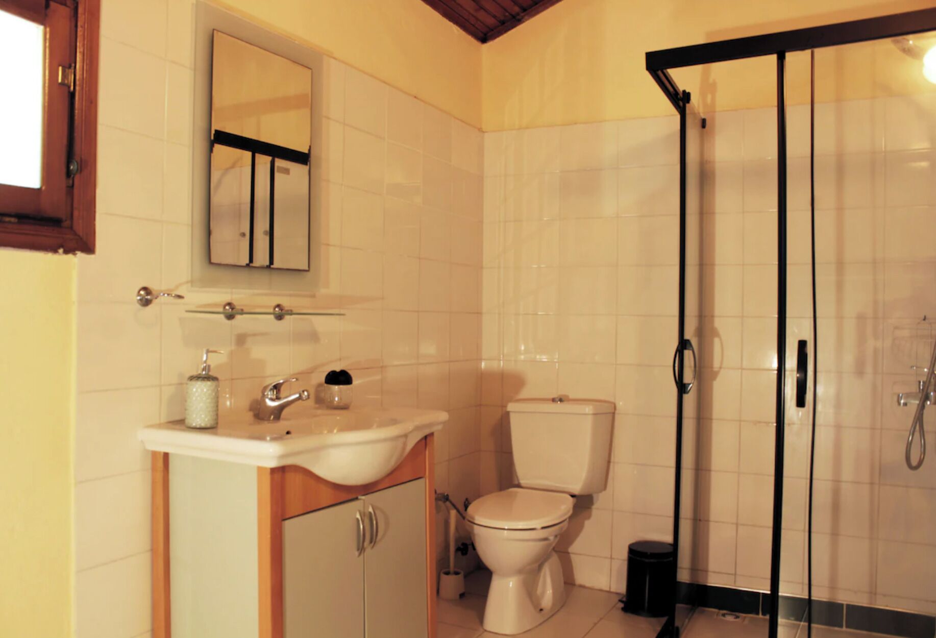 A bathroom with a toilet, sink, mirror, and shower enclosure.