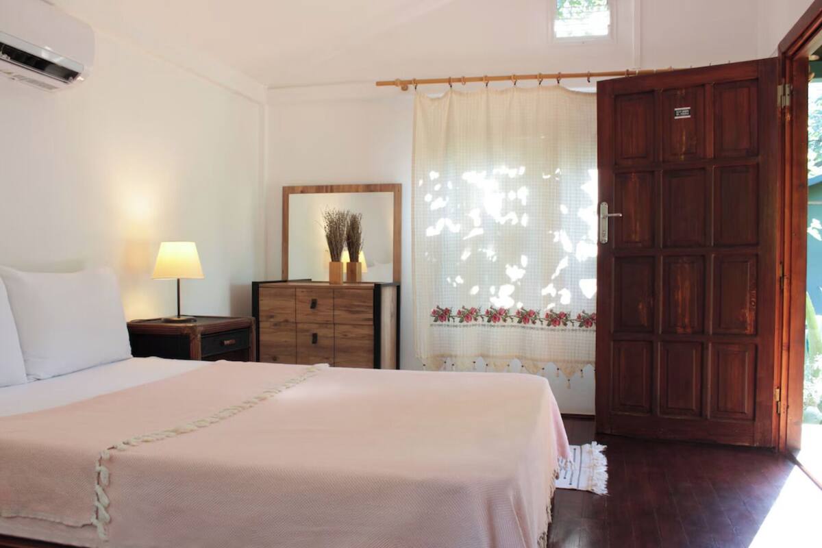 Une chambre à coucher avec un lit, une commode, un miroir, une fenêtre avec des rideaux et une porte en bois.