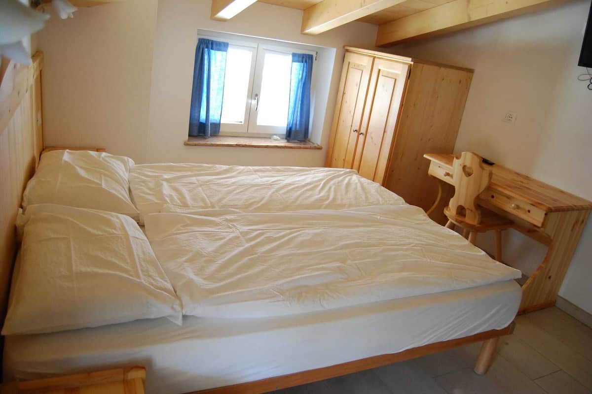 Une chambre à coucher avec un lit, une fenêtre avec des rideaux, une armoire en bois et un bureau.