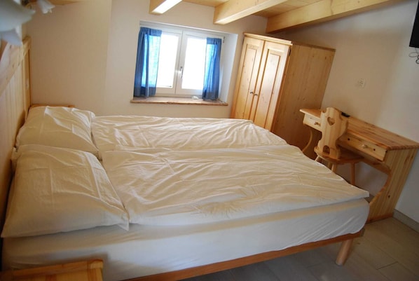 A bedroom with a bed, a window with curtains, a wooden wardrobe, and a desk.