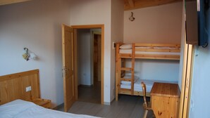 Ett rum med en enkelsäng, en våningssäng, en byrå i trä och en dörr som leder till ett annat rum.