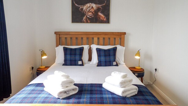 A hotel room with a wooden bed, blue and white bedding, a bull painting on the wall, and two bedside lamps.