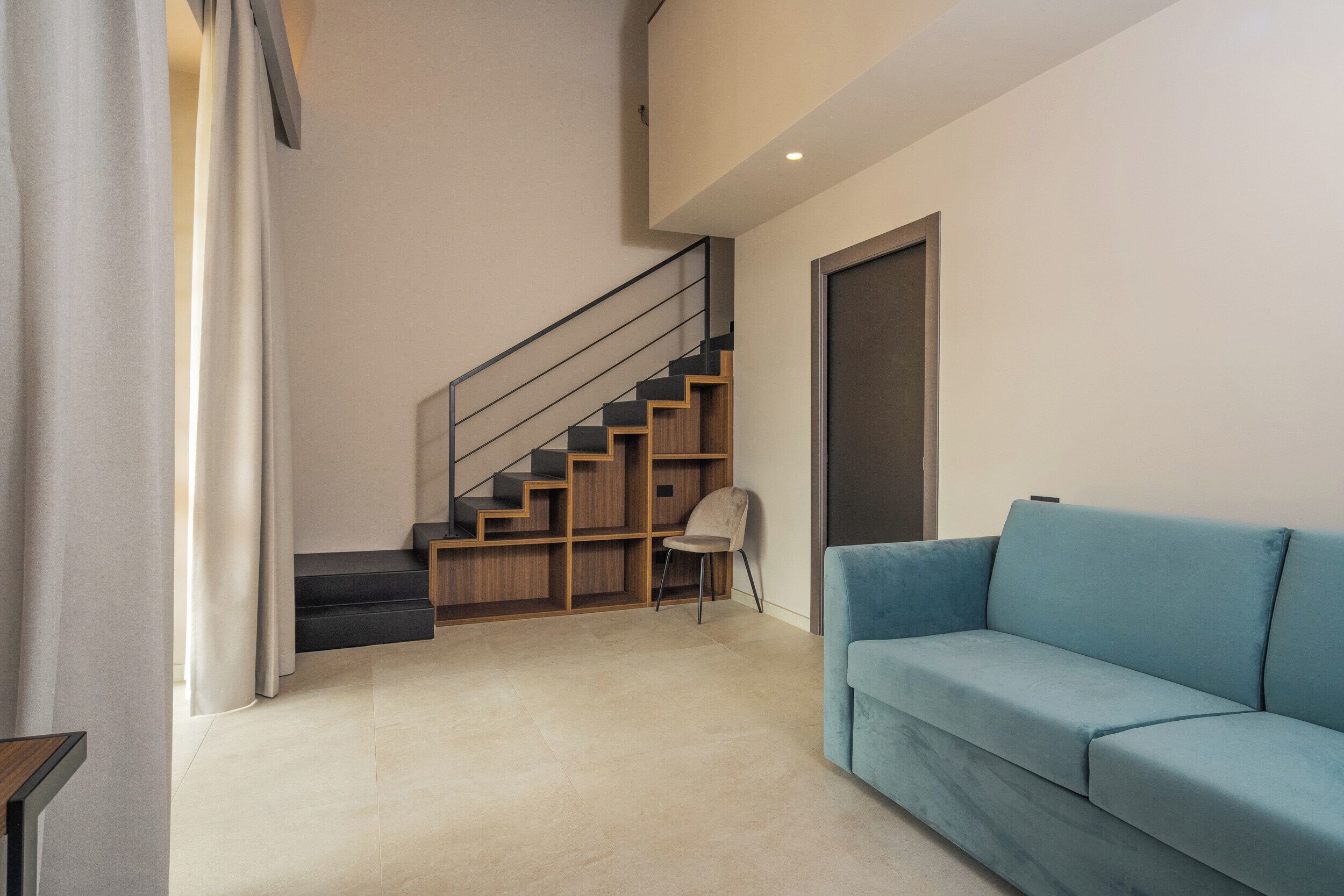 A modern interior with a staircase, a blue sofa, and a chair.