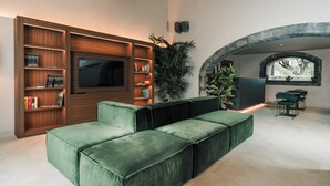 A modern living room with a sectional sofa, built-in wooden shelving, a flat-screen TV, and a stone archway. - Flora Sicula - Cultivating Hospitality (Giarre)