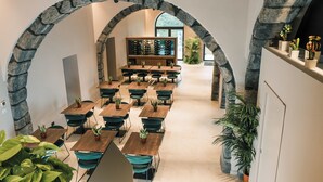 A modern interior with stone arches, wooden tables, and chairs, and a wine rack in the background. - Flora Sicula - Cultivating Hospitality (Giarre)