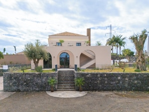 A two-story building with a stone wall in front, a staircase leading to the entrance, and a clear sky. - Flora Sicula - Cultivating Hospitality (Giarre)
