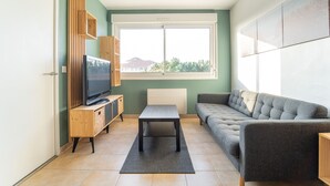 Ein modernes Wohnzimmer mit Fernseher, Sofa und Blick auf einen Berg durch ein Fenster.