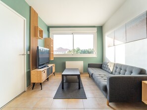 A modern living room with a television, sofa, and a view of a mountain through a window. - Central apartment - 4 guests (Mimizan)