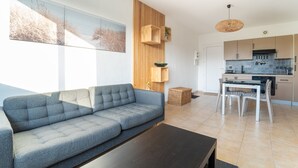 Ein modernes Wohnzimmer mit einem grauen Sofa, einem dunklen Couchtisch und einer Küchenzeile mit Holzschränken und einer Pendelleuchte.