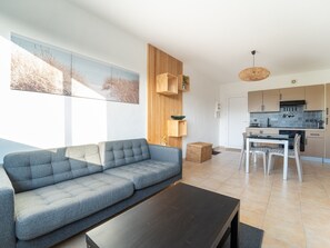 Een moderne woonkamer met een grijze bank, een donkere salontafel, en een keukenhoek met houten kastjes en een hanglamp.
